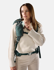Woman wearing a green backpack and holding a phone against a white background