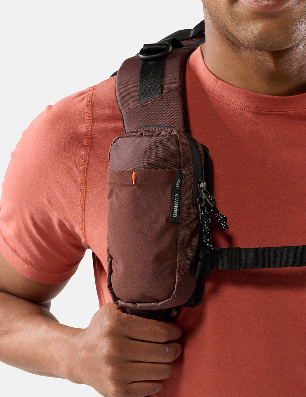 Person wearing a garnet crossbody bag on a plain background