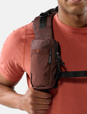 Person wearing a garnet crossbody bag on a plain background