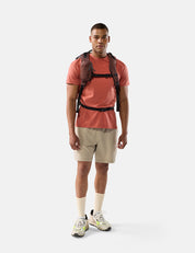 Man wearing a red shirt, beige shorts, and a garnet backpack on a white background