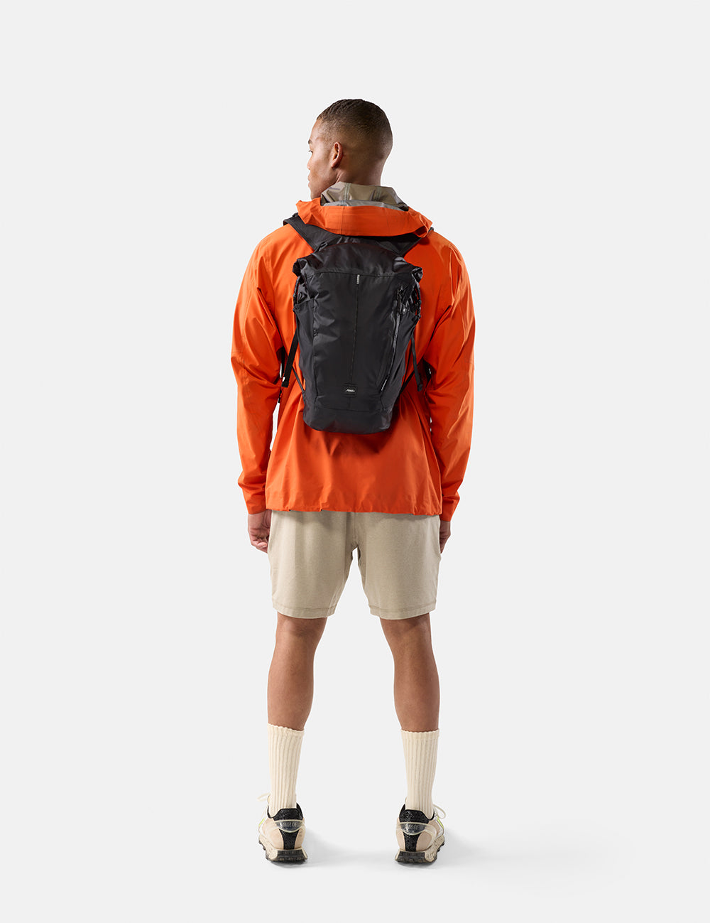Person wearing an orange jacket and black backpack on a white background