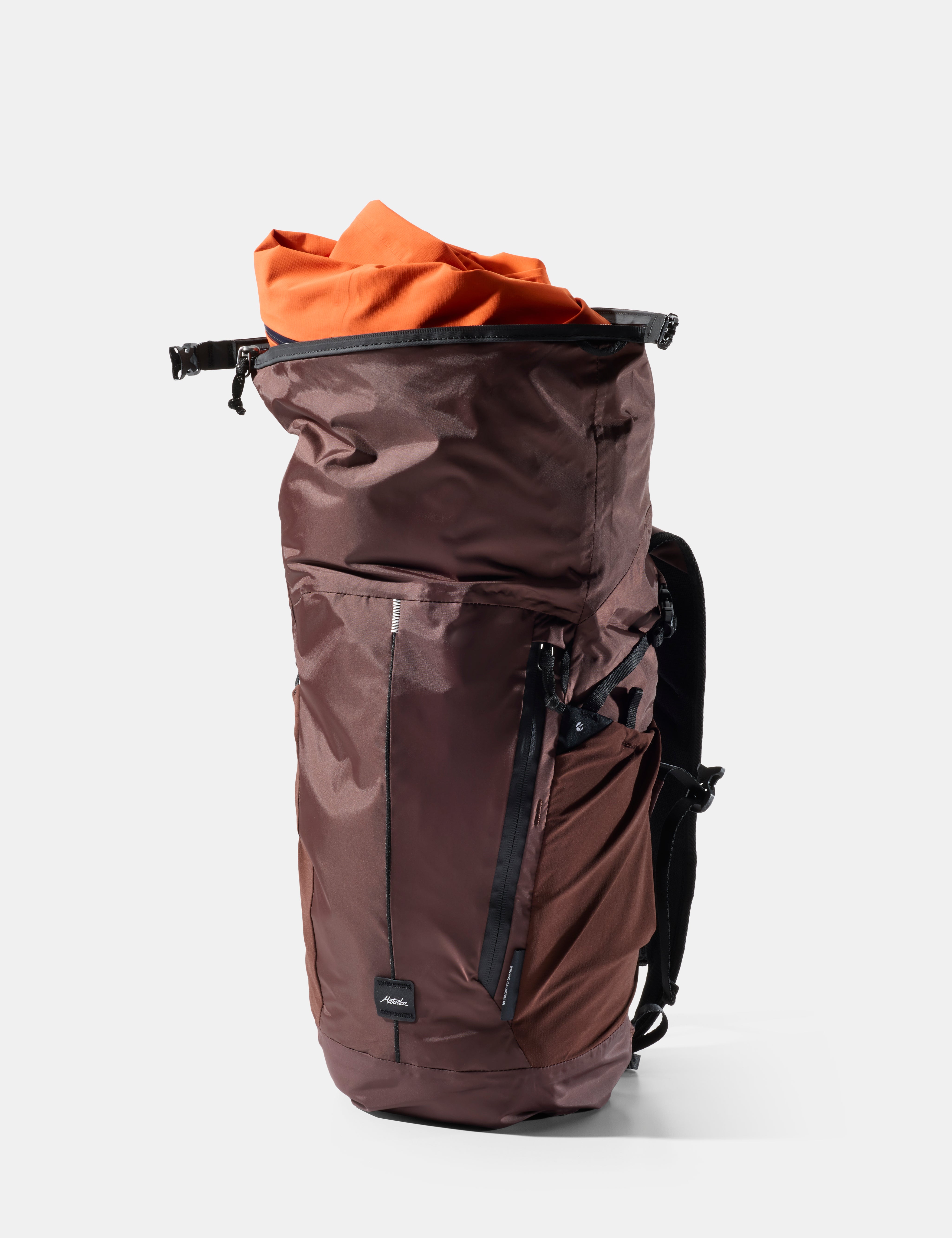 garnet backpack with orange rain jacket coming out the top on a white background