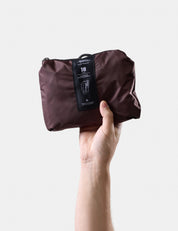 Garnet travel pack held by a hand with a visible brand tag on a light gray background