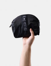 Black travel pack held by a hand against a light gray background
