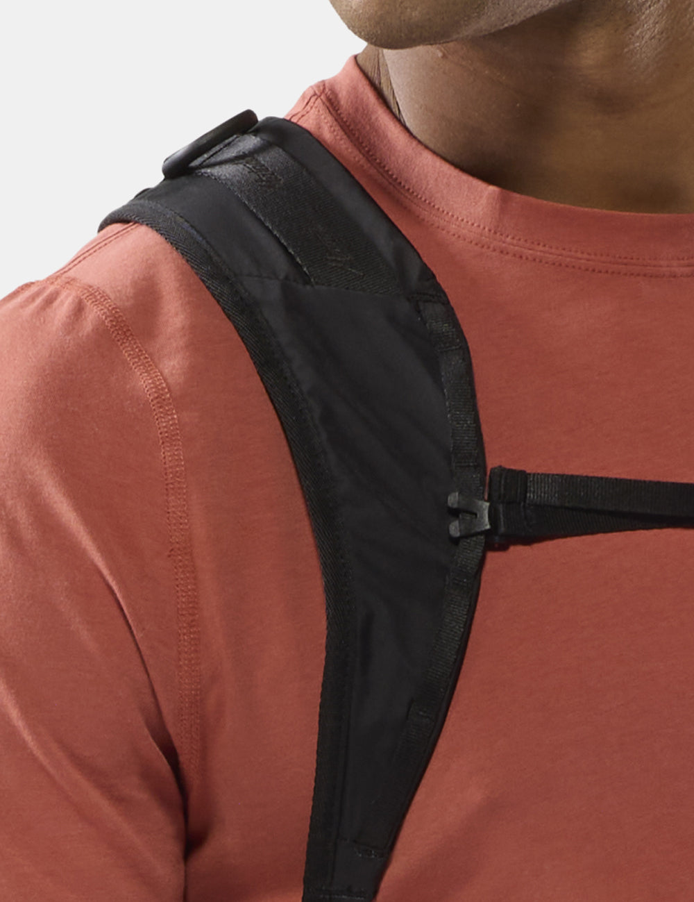 close up view of black backpack strap on person in orange shirt