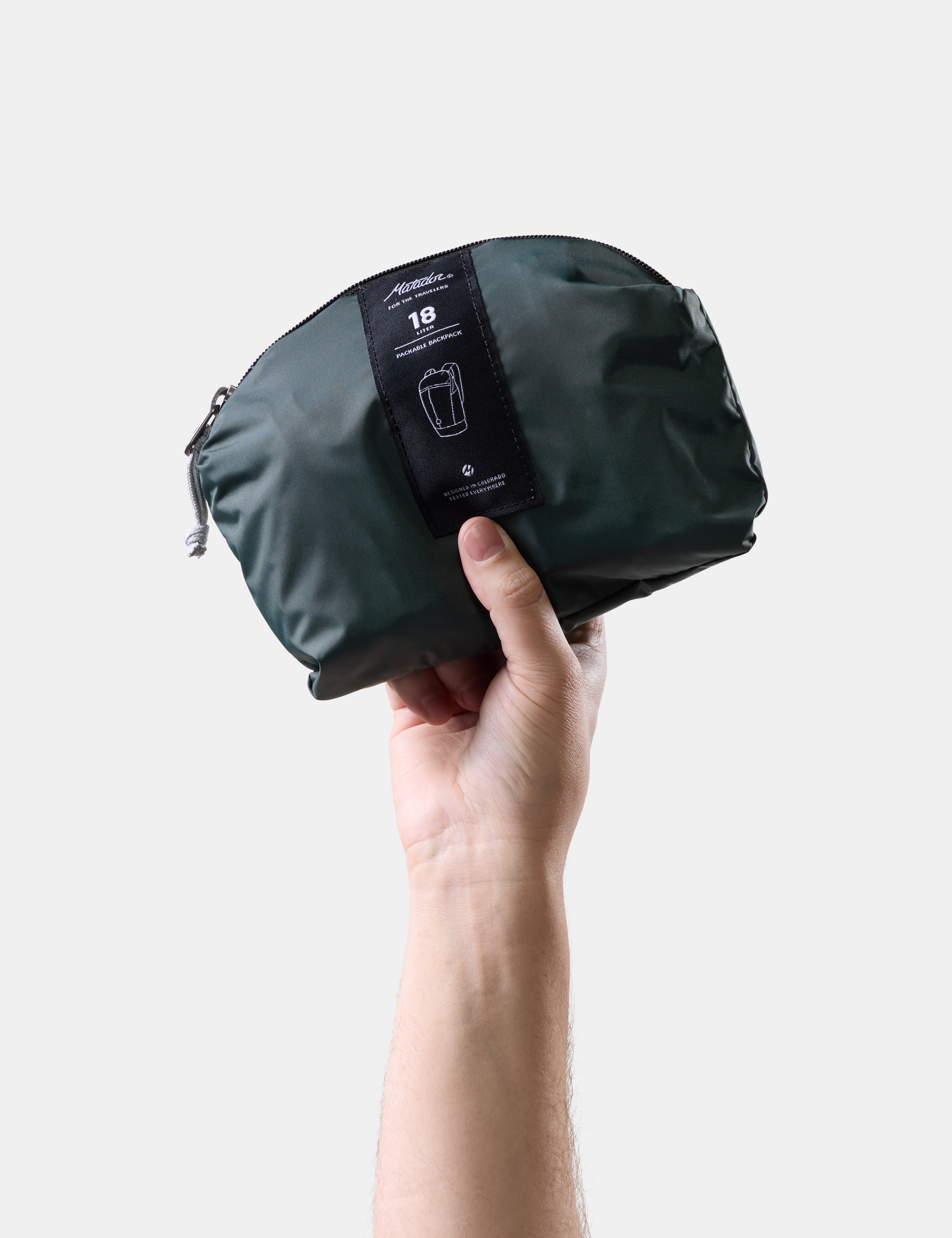Hand holding a juniper travel pack with a visible brand label on a light gray background