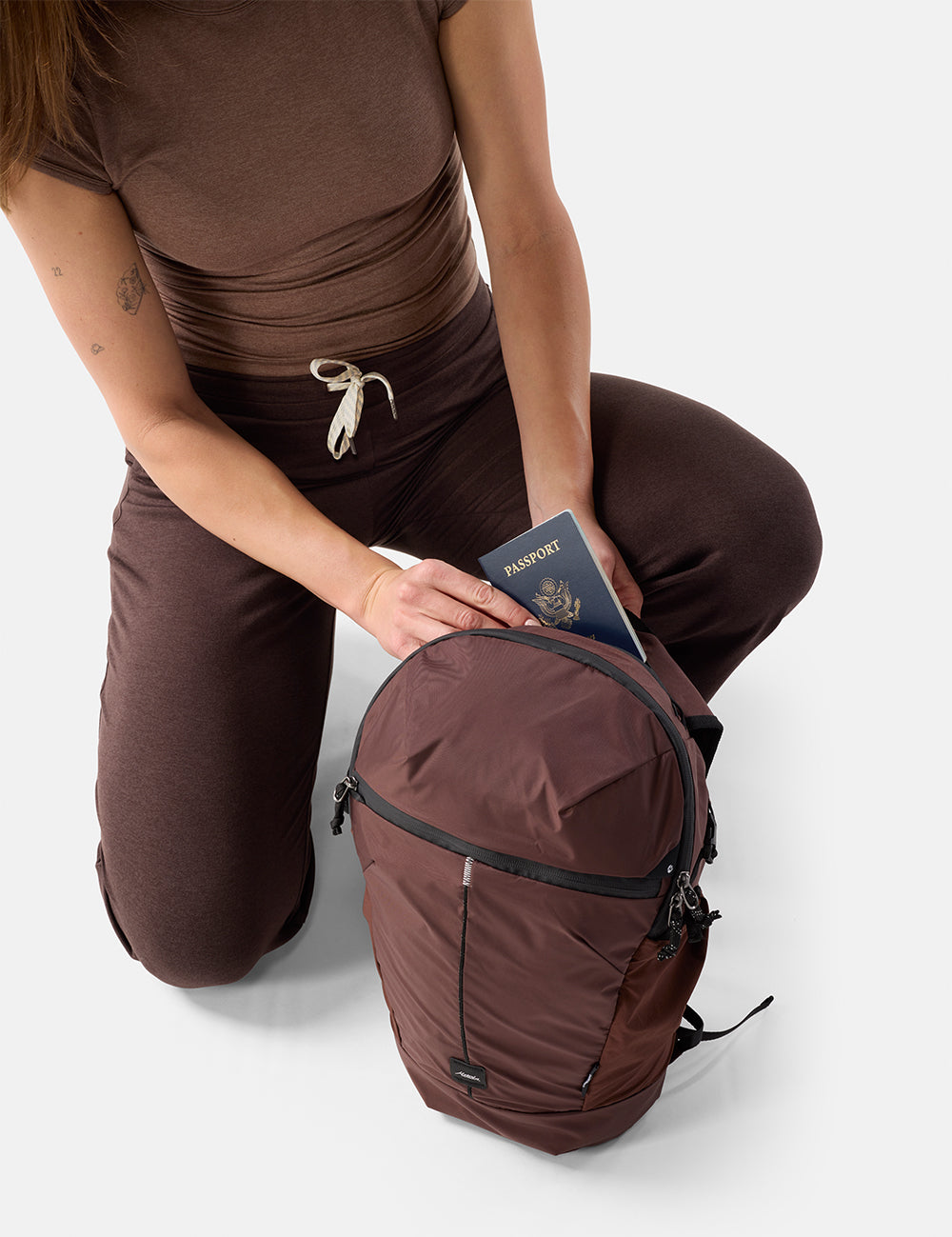 Person in brown outfit with a garnet backpack and passport on a white background