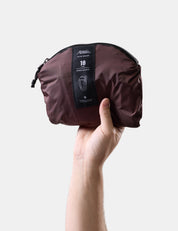 Hand holding a packed up garnet backpack with a label on a light gray background