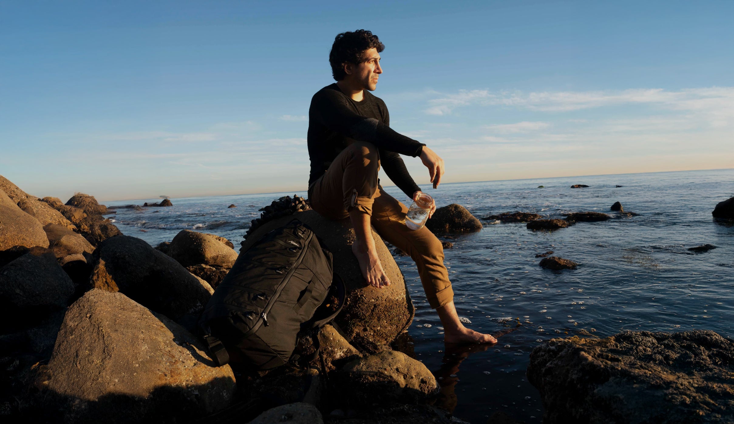 man sitting on rocks next to ocean with seg45 travel pack