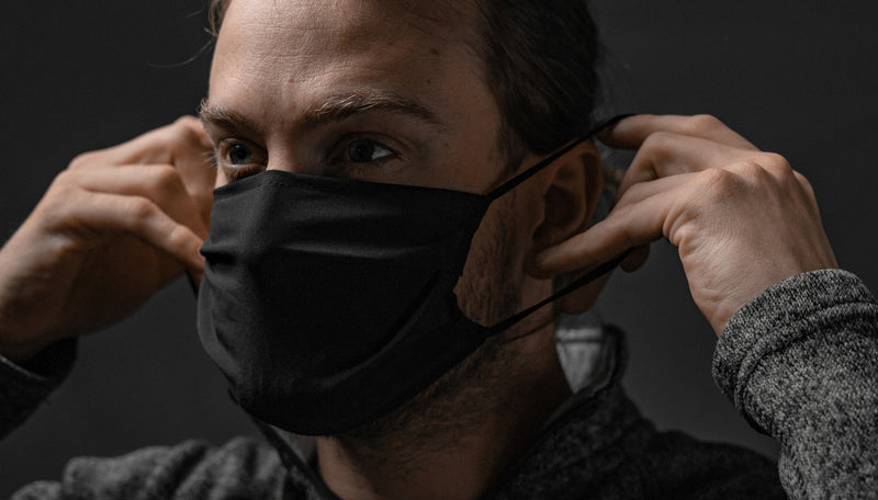 Man pulling black face mask ear loops behind his ears