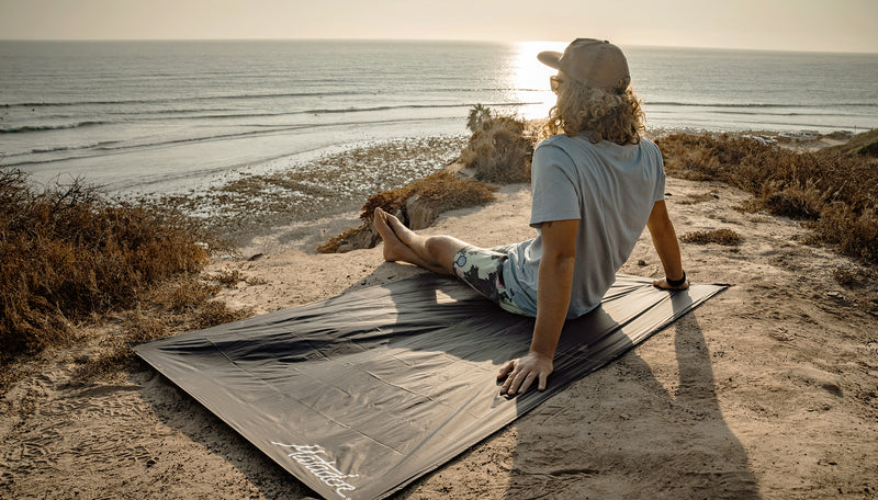 Man on sandy, sunset coastline, sitting on pocket blanket