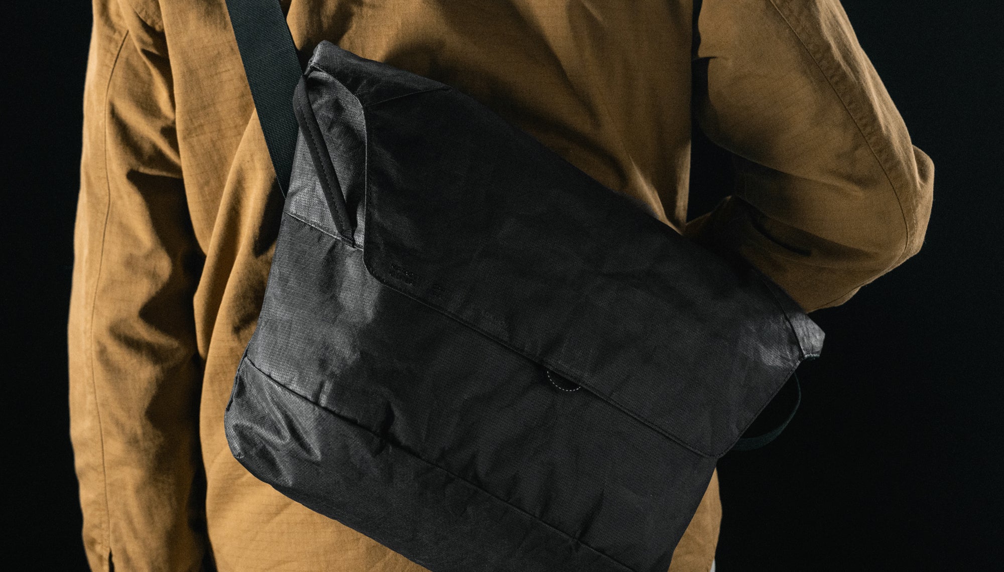 close up view of black messenger bag worn crossbody behind man