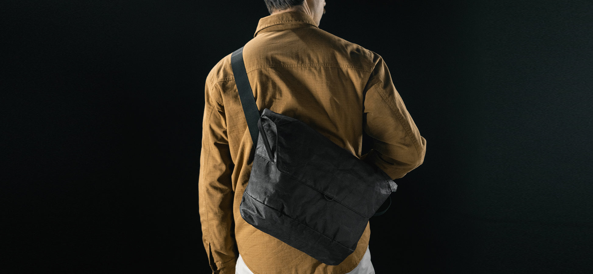 man in black studio wearing black messenger bag across his back