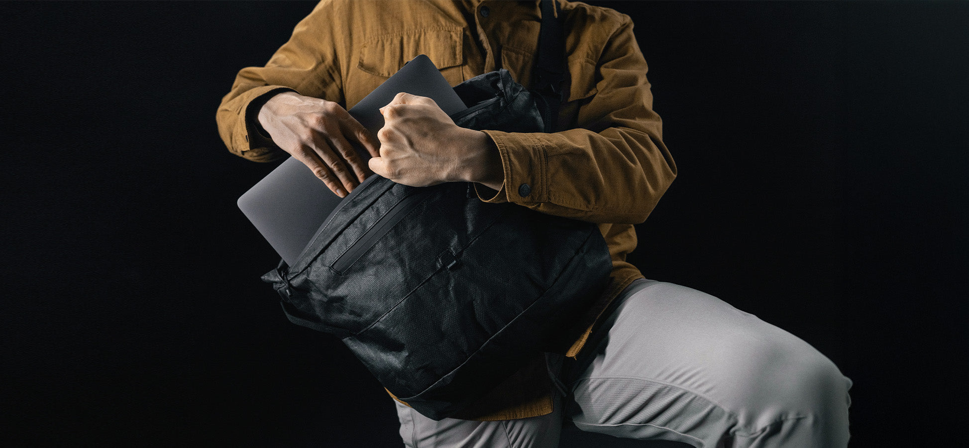 man in black studio, pulling laptop out of a black messenger bag