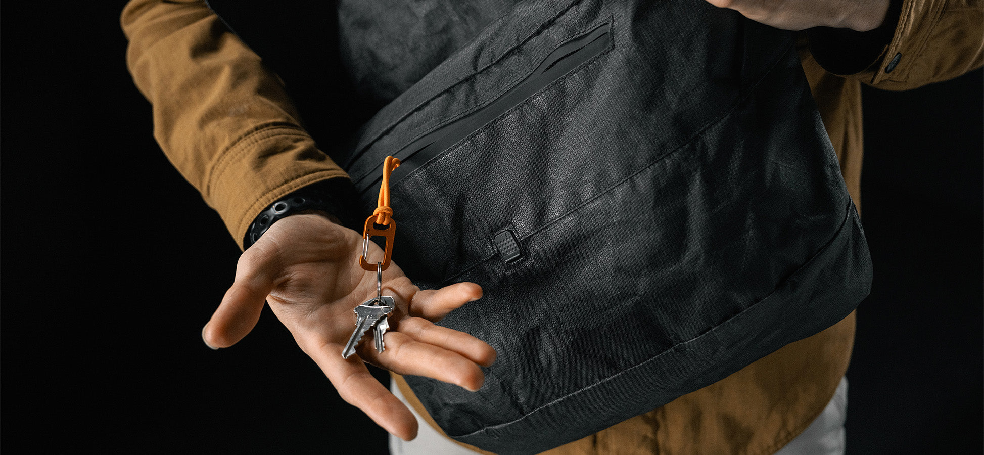 man pulling keys and orange carabiner out of black messenger bag