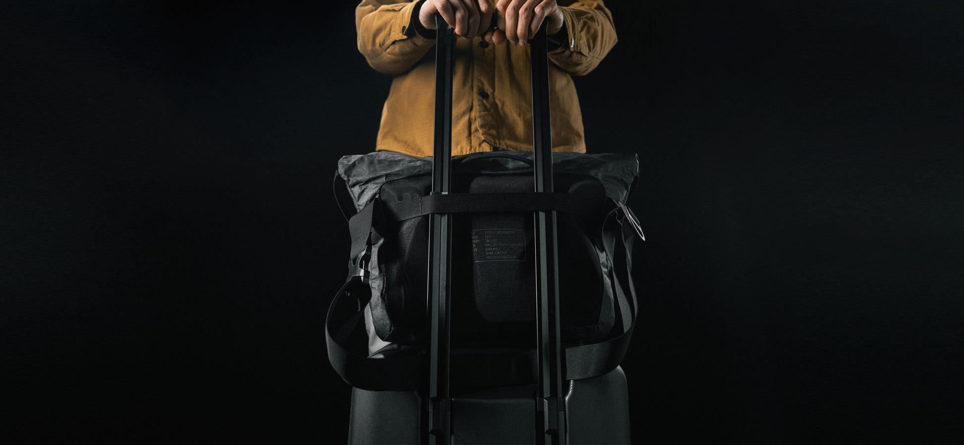 man standing with rolling luggage with black messenger bag attached to the handle