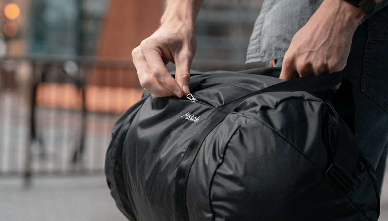 Man in city, unzipping side pocket of On-Grid Duffle