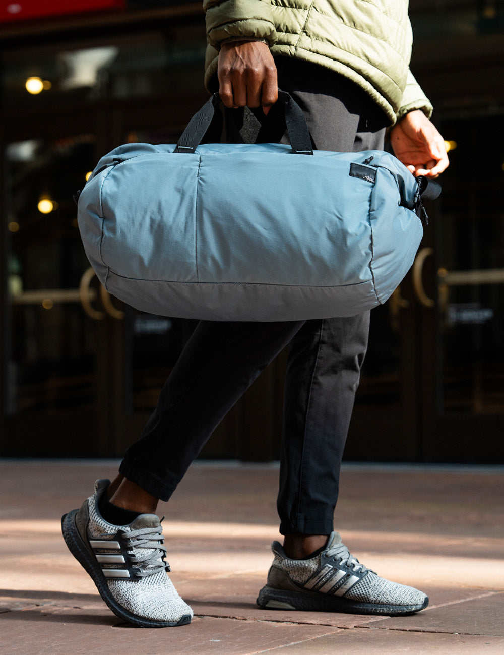 blue duffle being held by man walking on sidewalk
