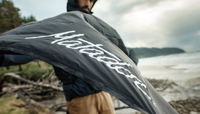 Man wearing raincoat on rocky beach, flapping open mini pocket blanket