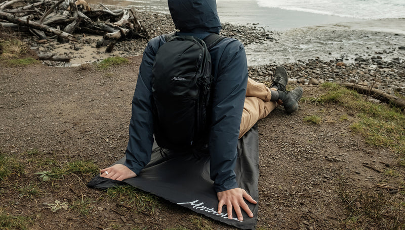 man in raincoat on rocky shore, sitting on pocket blanket mini