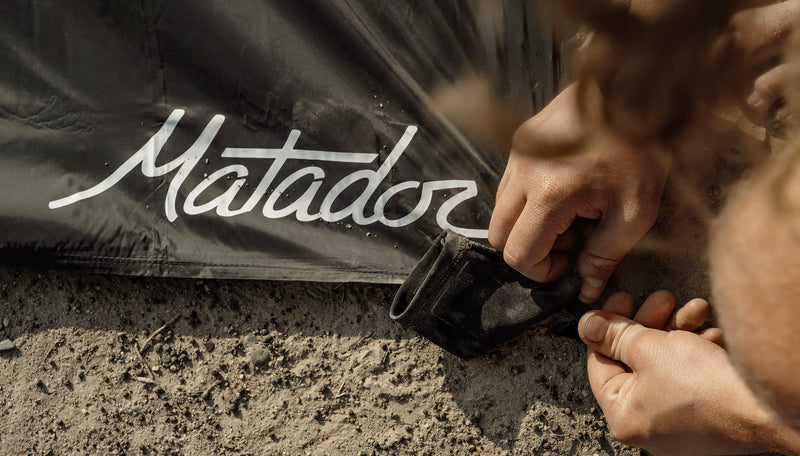 Matador logo corner of pocket blanket being staked to the ground