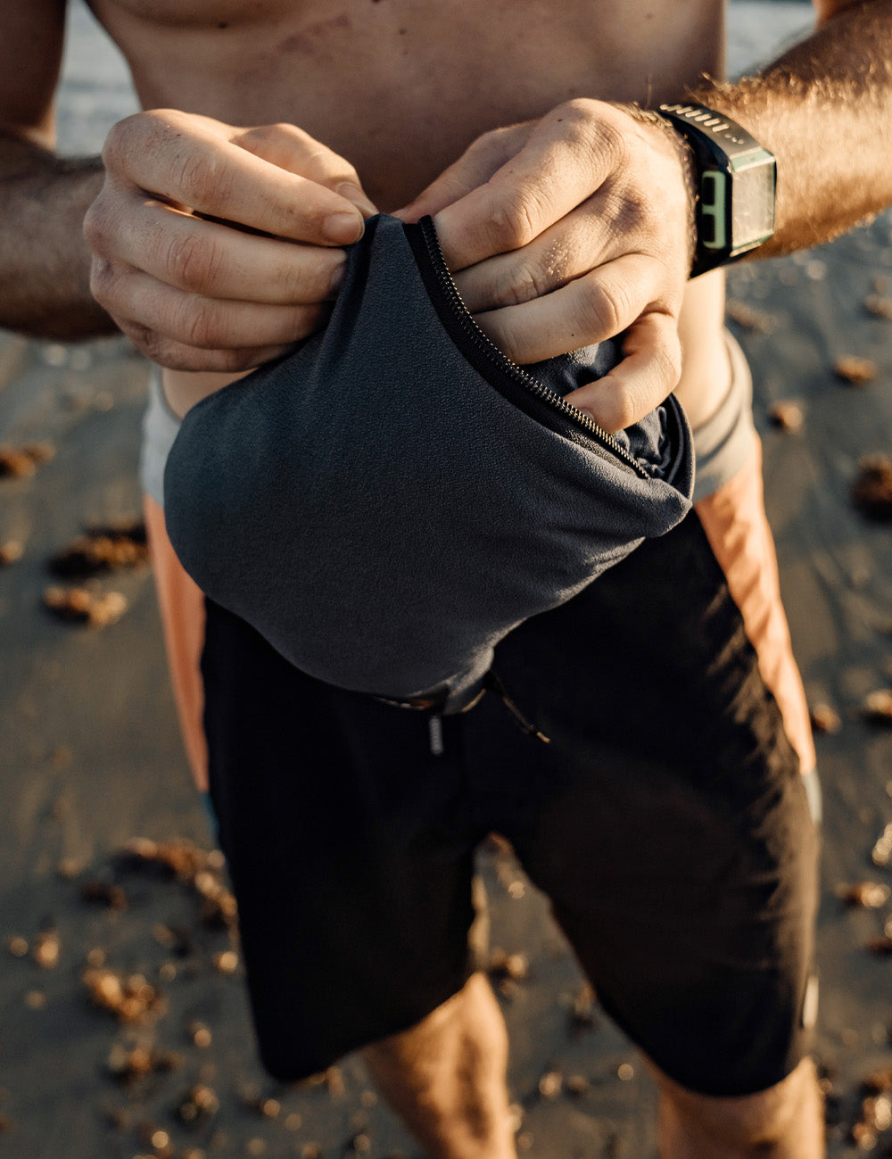Person on a beach holding a black pouch with a watch on their wrist.