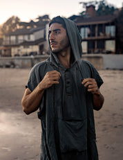 Man wearing a hooded garment on a beach with buildings in the background