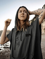 Person wearing a gray poncho with a brand logo on a beach