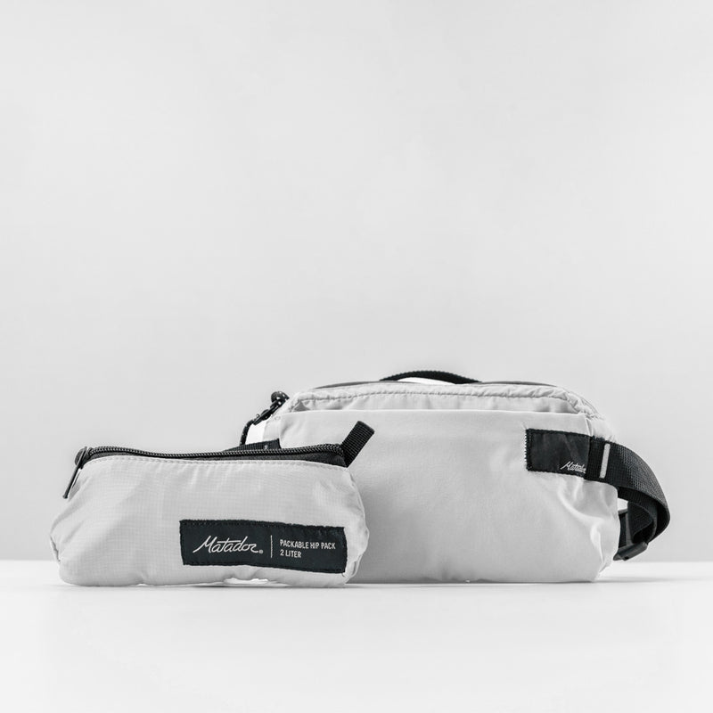 front view of white sling bag and packed up bag on light gray background