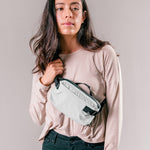 woman on light gray background wearing arctic white sling bag across the front of her body