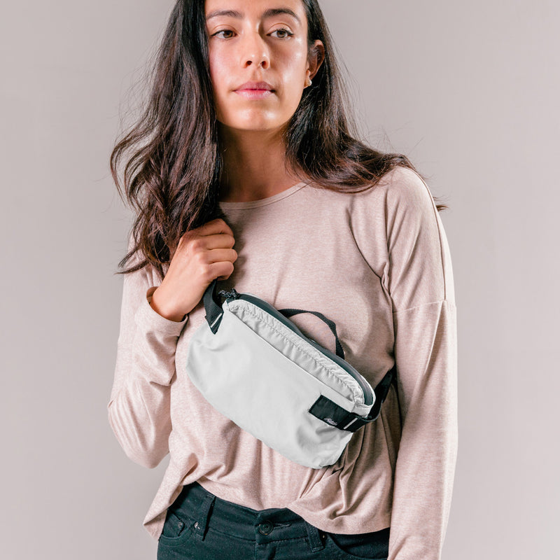 woman on light gray background wearing arctic white sling bag across the front of her body