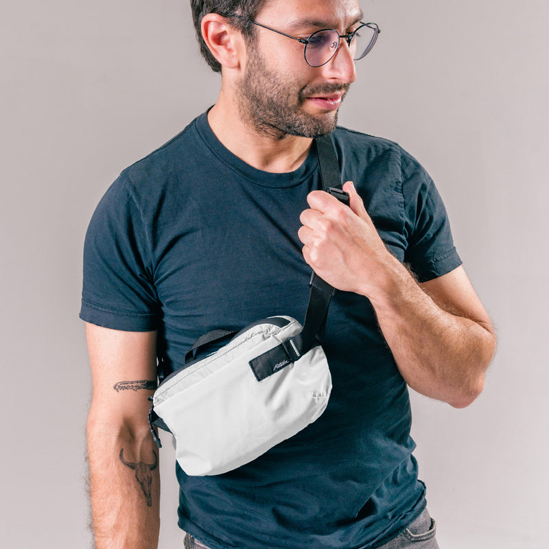 man on light gray background wearing arctic white sling bag across the front of her body