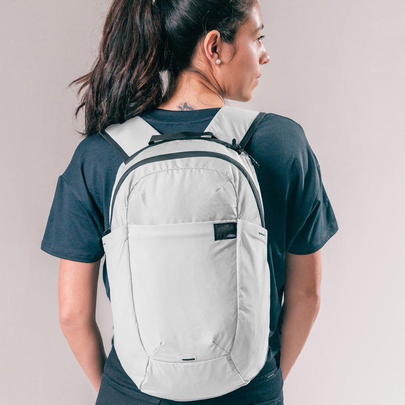 back view of woman wearing arctic white backpack on light gray background