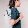 side view of woman wearing arctic white backpack on light gray background