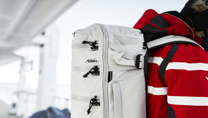 Close up view of white SEG28 backpack worn by a man in a red jacket, looking over the deck of an arctic ship