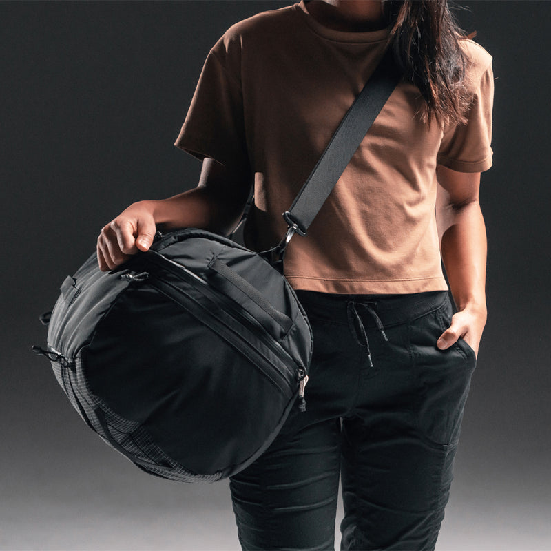 Woman on dark gray background, carry SEG45 as a duffle across her body