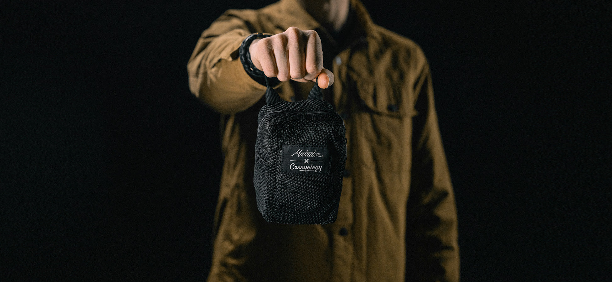 man in black studio holding packed up sling bag 