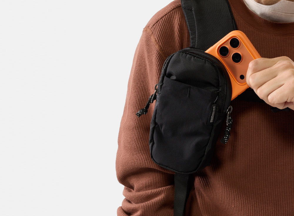 person pulling orange phone out of black backpack strap pocket
