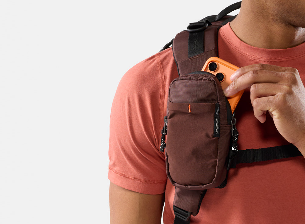 person pulling orange phone out of garnet backpack strap pocket