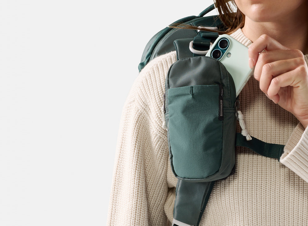 person pulling green phone out of juniper backpack strap pocket