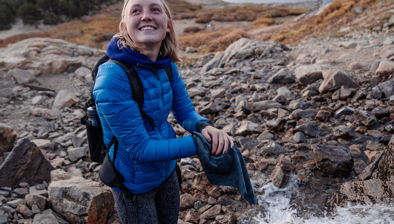 woman in blue puffy jacket, drying hands with ultralight towel at rocky stream