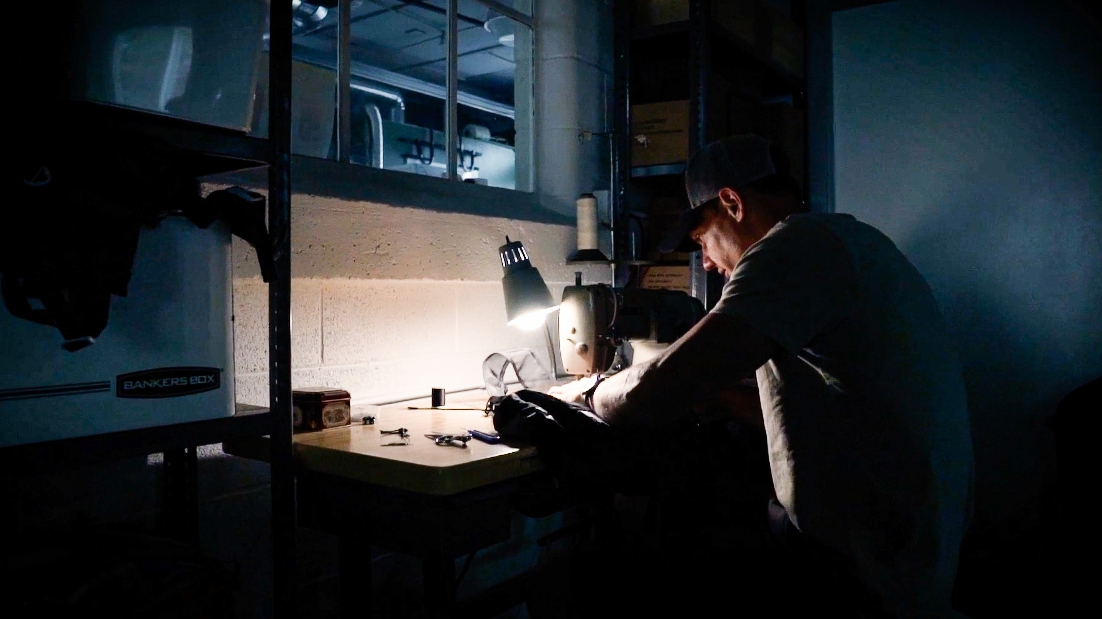 Man in dark room, sitting at lit up sewing machine