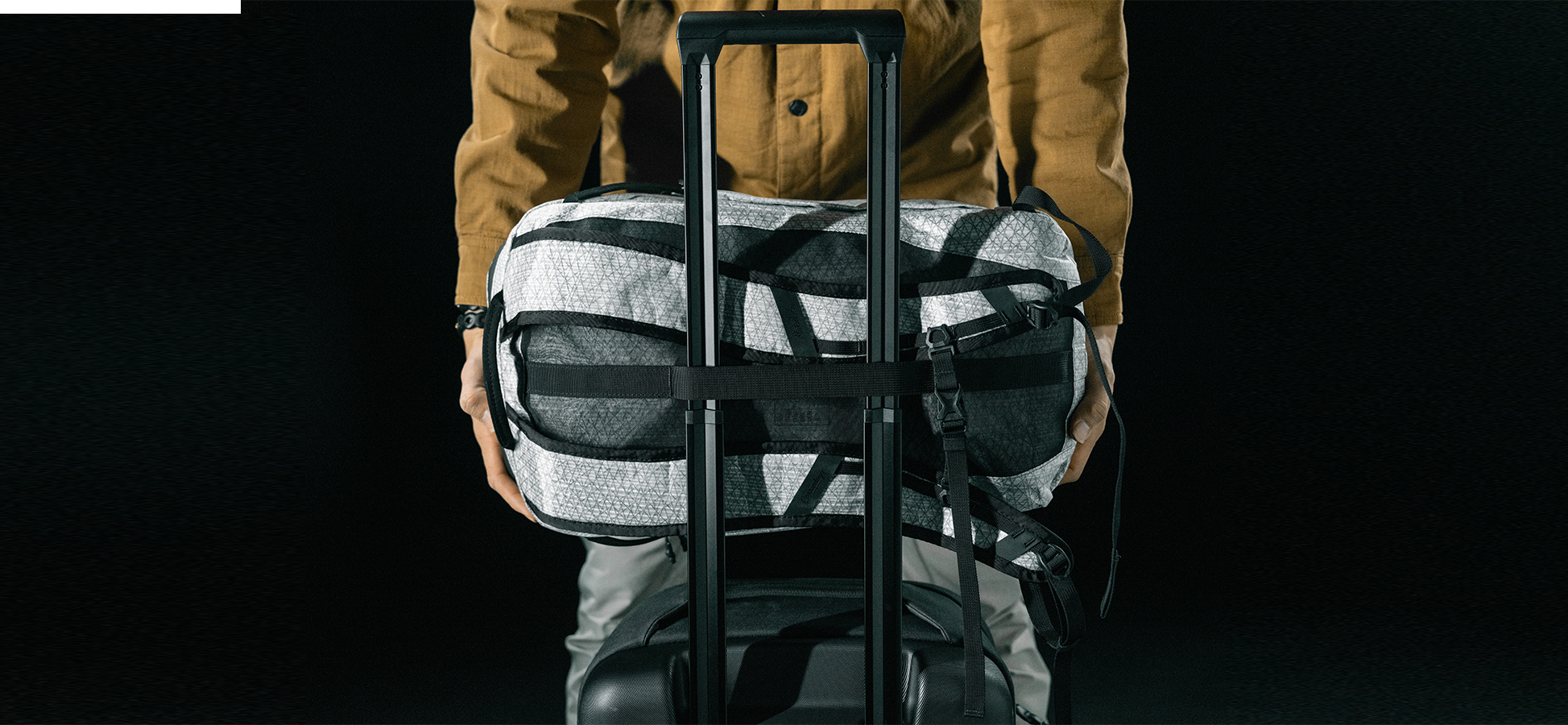 man placing white backpack onto rolling luggage arm