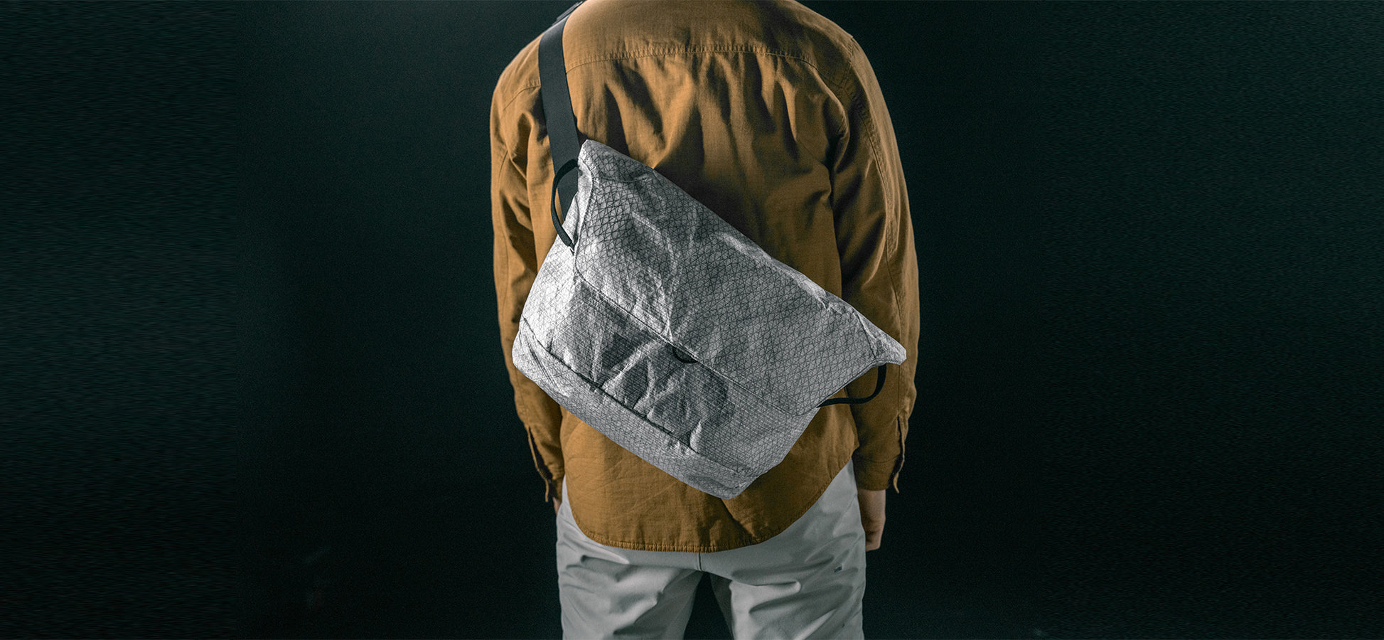 man in black studio wearing white messenger bag across his back