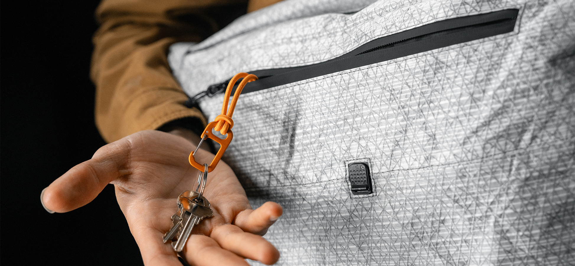 man pulling keys and orange carabiner out of black messenger bag