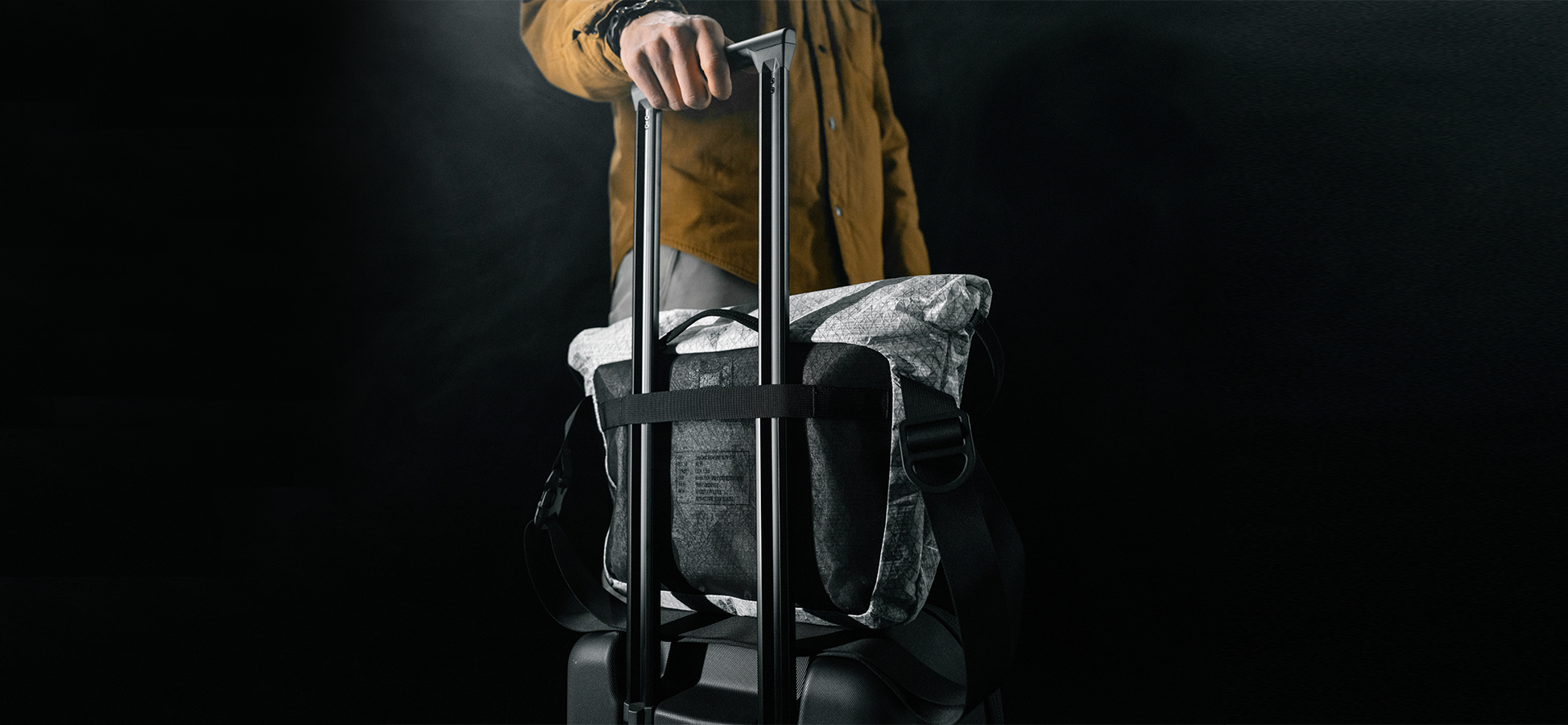 man standing with rolling luggage with white messenger bag attached to the handle