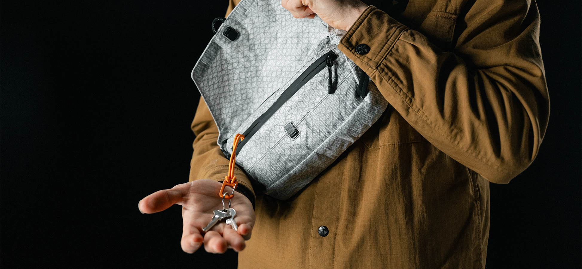 man pulling keys and orange carabiner out of white sling bag