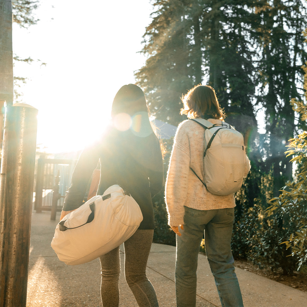 two women walking into sunshine with white duffle and backpack