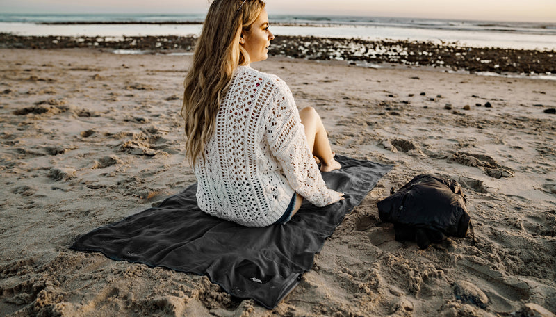 woman sitting on beach on top of charcoal beach towel