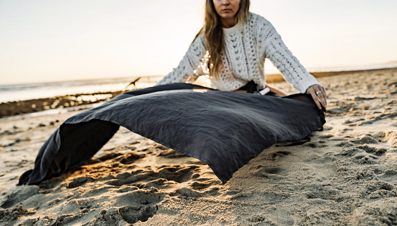 woman on sandy beach, laying out charcoal beach towel